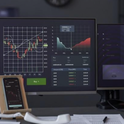 A trading desk setup with multiple monitors displaying financial graphs and a smartphone placed on the desk